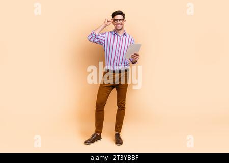 Full length photo of cheerful nice man dressed stylish clothes hold modern gadget ipad working online isolated on beige color background Stock Photo