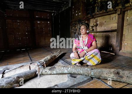 Woman from Adi tribe in traditional clothes sitting by the fireplace in traditional wooden house in Assam, Northeast India Stock Photo