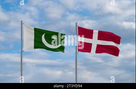 Denmark and Pakistan flags waving together on blue cloudy sky, two country relationship concept Stock Photo