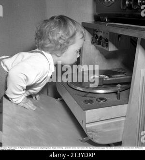Child at a gramophone in the 1950s. The little boy is fascinated by the revolving record spinning and looks as if he is about to touch it. Sweden 1950. Conard ref 1525 Stock Photo