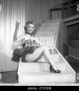 A woman in the theater in the 1950s. A young woman from the theater ballet sits on a step dressed in her stage clothes. The picture was taken at a Stockholm theater where you can glimpse the theater backdrops. She smiles and waves. Surely an eye catcher for the male audience as she has a beautiful appearance. Sweden 1951. Kristoffersson ref BC48-8 Stock Photo