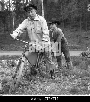 In the 1950s. A man pictured when trying to balance himself on a bicycle and is given help by his son who holds the bike straight. Sweden 1951. Kristoffersson ref BP30-6 Stock Photo