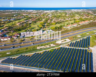 Solar power plant row at sunset and Cocotal residence on the seashore in the background. Farm producing clean electrical energy Stock Photo