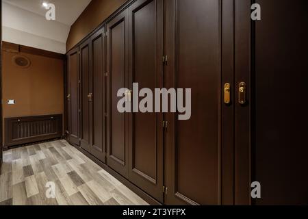 Access hallway to the dressing room with access to numerous built-in wardrobes with brown wooden doors, a radiator cover integrated into the wall and Stock Photo