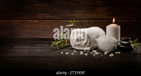 wellness spa background. body skin care items on dark wooden table. towel, bath crystals, massage stones and candle. banner with copy space Stock Photo