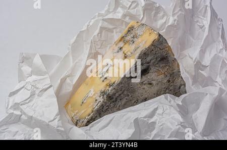 triangular piece of cheese with mold on white crumpled paper close-up Stock Photo