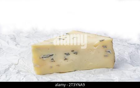 triangular piece of cheese with mold on white crumpled paper close-up Stock Photo