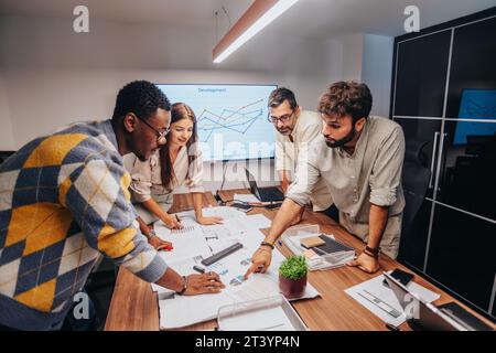 Multiracial Team of Architects and Engineers Discussing Blueprint in Business Meeting Room Stock Photo