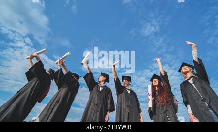 Cheerful graduates waving their diplomas on a sunny day. Stock Photo