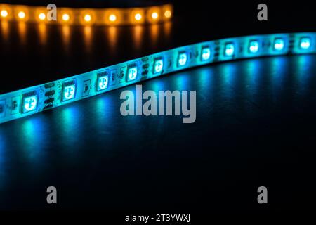 Bobbin with roll of glowing LED strip lighting placed on table, pink, and warm white,blue color in dark room Stock Photo