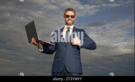 Happy programmer holding laptop. Computer programmer showing thumb gesture. Hardware programmer Stock Photo