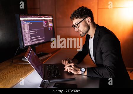Young man mobile developer writes program code on a computer, programmer work in home office. Stock Photo