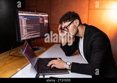 Young man mobile developer writes program code on a computer, programmer work in home office. Stock Photo