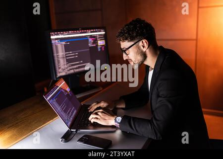 Young man mobile developer writes program code on a computer, programmer work in home office. Stock Photo