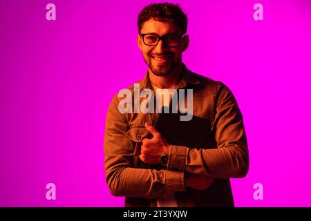 Cheerful happy young man using modern digital tablet and wireless stereo headphones, playing video game, watching video content online on red studio b Stock Photo