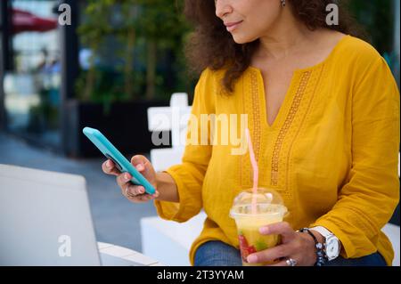 Close-up view of a charming woman, business lady checking her smart mobile phone, sitting at an outdoor cafes and working online on laptop computer, h Stock Photo