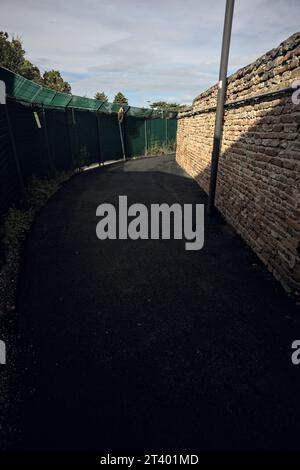 Bend  in a gravel path between a fence and a brick wall on a cloudy day Stock Photo