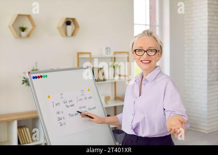 Happy online English teacher standing by white board and explaining grammar rules Stock Photo