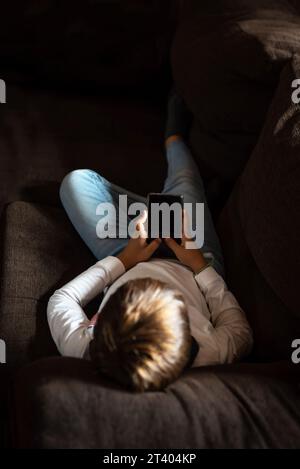 A child lying on the couch, staring at a mobile phone. Addiction and dependence of children and youth on new technologies. Parents' concern about chil Stock Photo