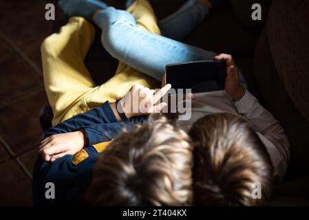 Two children lying on the couch, staring at a mobile phone. Addiction and dependence of children and youth on new technologies. Parents' concern about Stock Photo