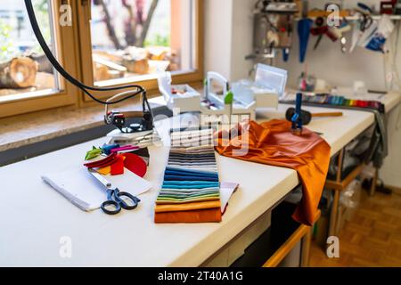 sewing or tailoring workshop showcases a table filled with sewing essentials: fabric swatches, scissors, iron, color palette, silk fabrics and tools, Stock Photo