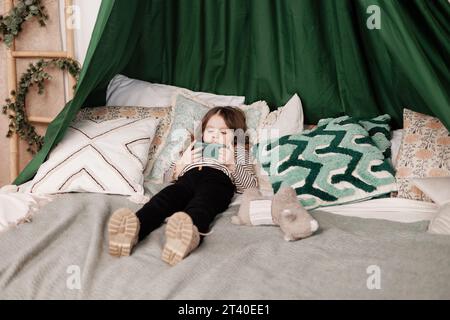Children's internet addiction. Little child girl plays video games or watches online videos on smartphone on bed in room. Virtual life. Psychological Stock Photo
