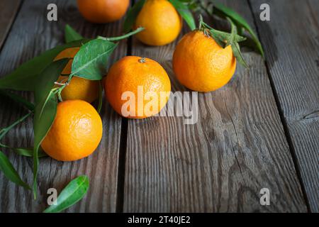 Tangerines (oranges, clementines, citrus fruits) with leaves on a wooden background. Mandarin oranges with leaves. Stock Photo