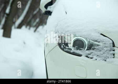 car headlight with lens xenon light covered with snow in winter weather, snowdrifts on the road. close-up of a vehicle detail. Stock Photo