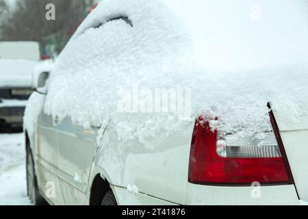 car rear headlight with red stop signal covered with snow in winter weather, snowdrifts on the road and of other automobiles. close-up of a vehicle de Stock Photo