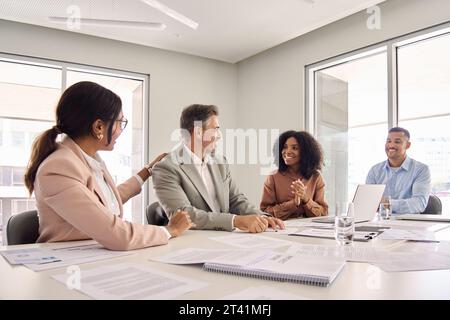 Happy executive team congratulating older leader celebrating success at meeting. Stock Photo