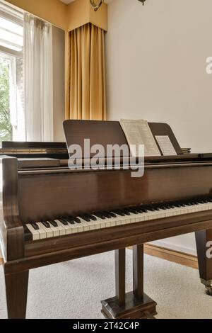 a living room with a piano on the floor and windows in the photo is taken from inside, while it's still showing Stock Photo