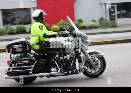 A police officer wearing a blue uniform parked on his motorcycle in a commercial parking lot Stock Photo