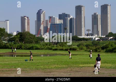 Children play baseball on a flooded field next to the Tama River with the tall buildings of Musashi Kosugi behind. Tokyo, Japan, Stock Photo