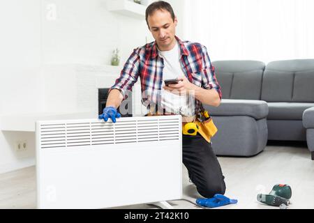 Workman mounting water heating radiator near the window in the white renovated living room, Image with copy space Stock Photo