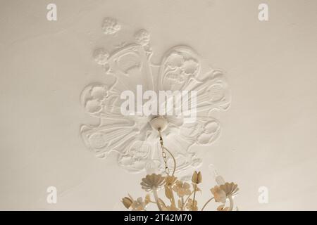 flowers in a vase on a table with a white wall behind it and a butterfly hanging from the ceiling above Stock Photo