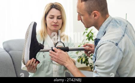 Modern Hospital Physical Therapy: Doctor Uses Tablet Computer, Helps Disabled Patient with Injury Walk on Treadmill Wearing Advanced Robotic Stock Photo