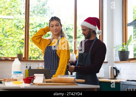 Happy caucasian couple putting on aprons, christmas baking in kitchen Stock Photo
