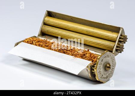 An Evans Patent Concinnum Machine, a vintage cigarette rolling device.  Internal view, showing the brass rollers with tobacco and a cigarette paper. Stock Photo