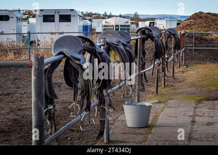 Horse saddles hanging in row on the stable fence. Stock Photo