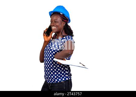young female construction engineer holding clipboard and talking on mobile phone while smiling. Stock Photo