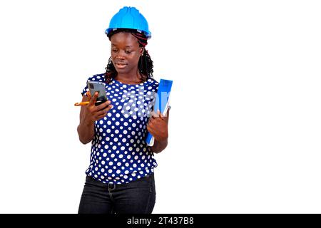 beautiful young female construction engineer holding clipboard and using mobile phone. Stock Photo