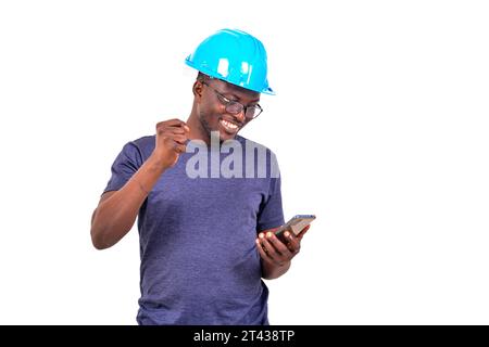 portrait of a happy young male construction engineer wearing a blue hard hat using a mobile phone while smiling. Stock Photo