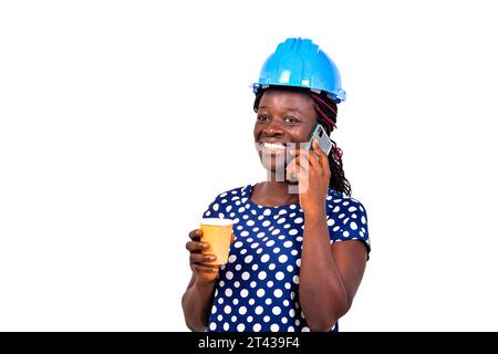 young female construction engineer wearing blue hard hat holding paper coffee cup and talking on mobile phone while smiling. Stock Photo
