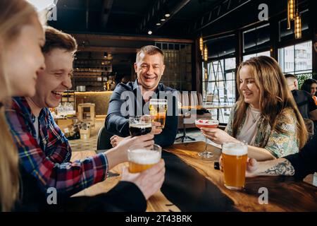 Group of happy relaxing friends drinking beer and coctails and having talk in pub restaurant Stock Photo