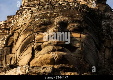 A huge face carved in stone, seen from below, low angle shot, illuminated by the afternoon light at Bayon temple, Angkor, Cambodia. Stock Photo