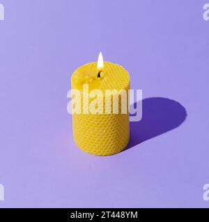 Creative layout of beeswax candle made with natural wax produced by honey bees on pastel violet background. Minimal concept. Trendy beeswax candle. Stock Photo