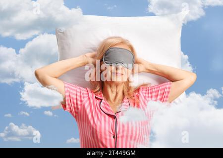 Woman in pajamas with a mask on eyes sleeping on a pillow between clouds and blue sky Stock Photo