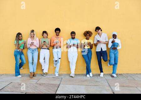 Multi-ethnic young people leaning on a wall using phone Stock Photo