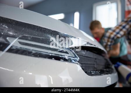 Technician covering car body with protective film at vehicle detailing service Stock Photo