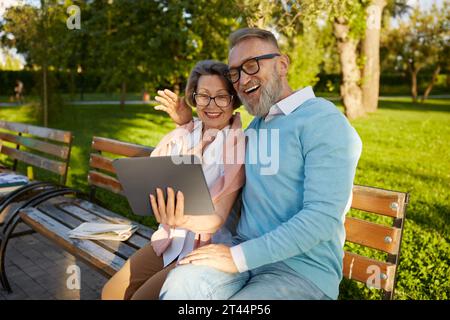 Smiling senior couple having videocall using digital tablet on park bench Stock Photo